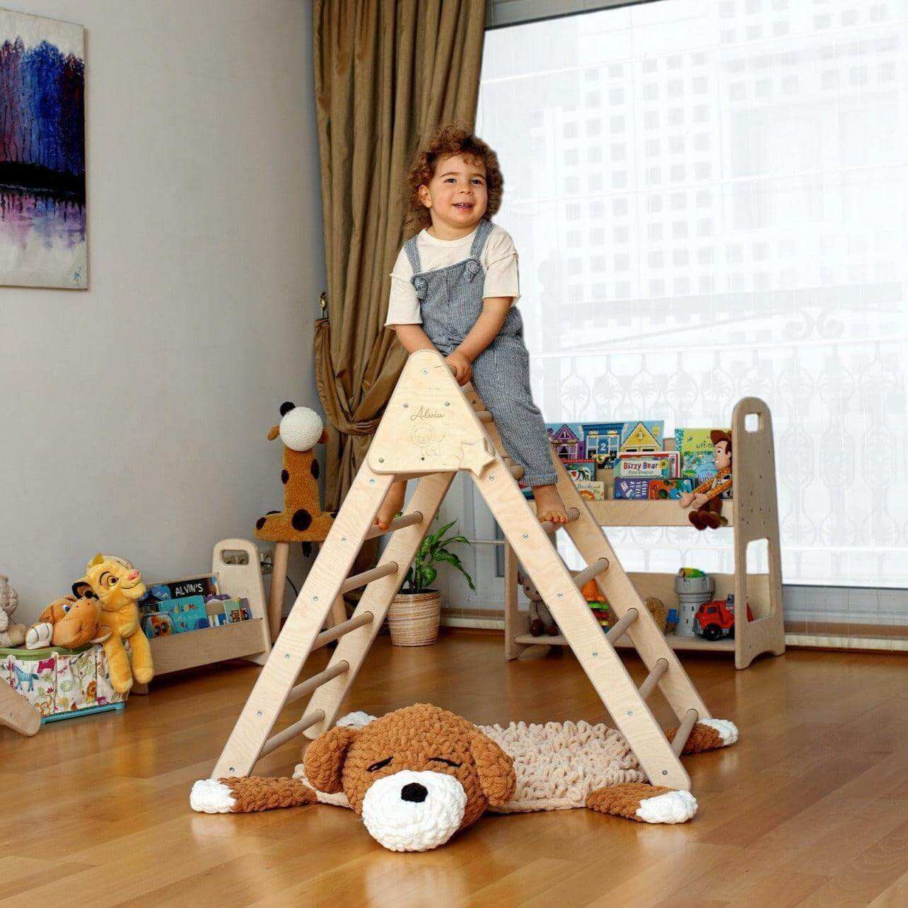 Toddler climbing on a natural wood Montessori Triangle Climber Set indoor playground with stuffed toy in a cozy playroom