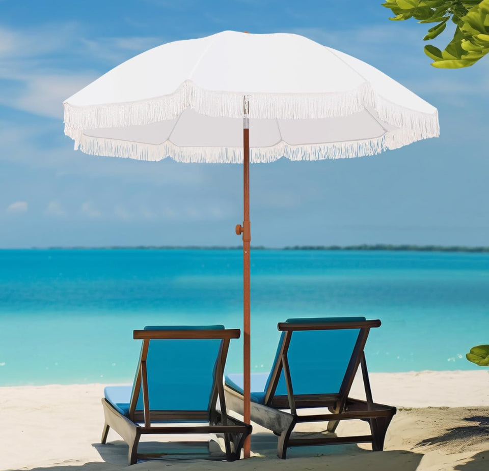 White patio umbrella with UPF 50+ protection and fringe detail shading two blue beach chairs by the ocean