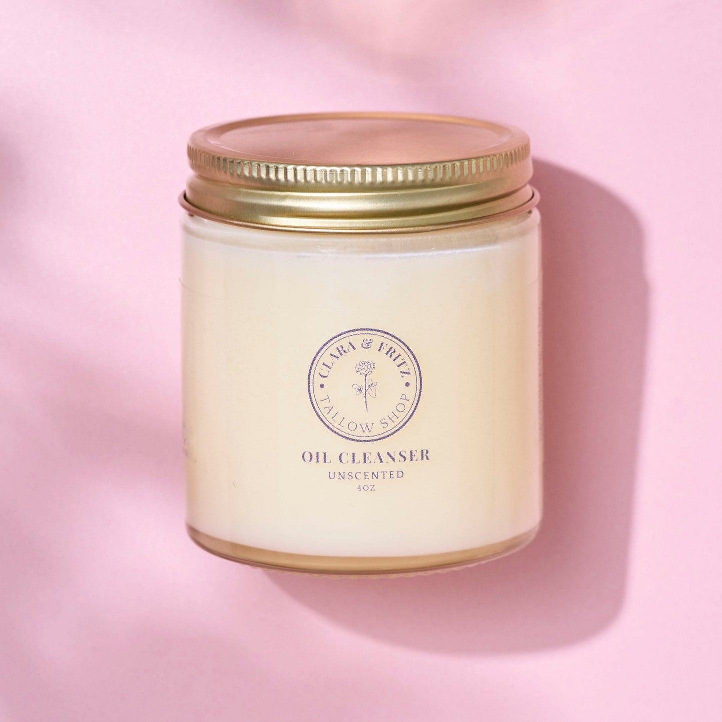 Tallow-based oil cleanser jar with gold lid on pink background, unscented natural skincare product for hydration and gentle cleansing