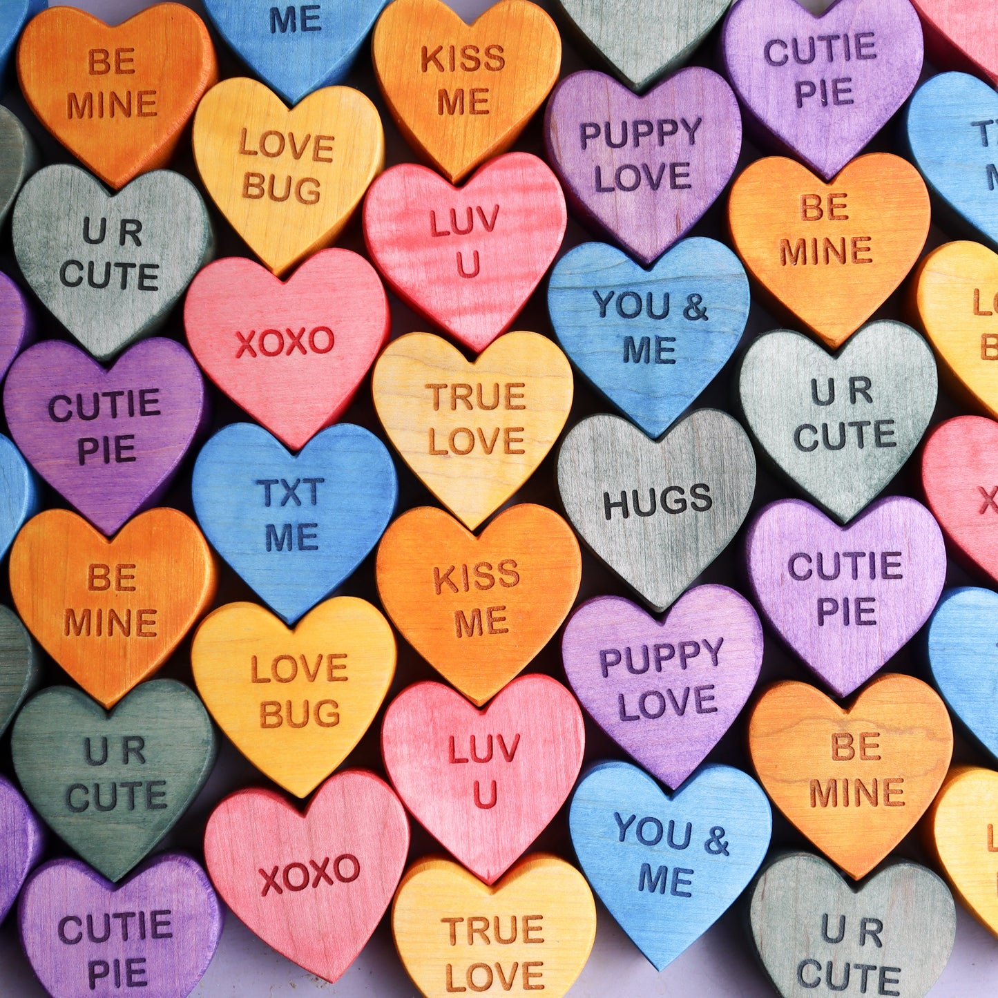Colorful wooden candy hearts with engraved love messages in various pastel shades arranged closely together