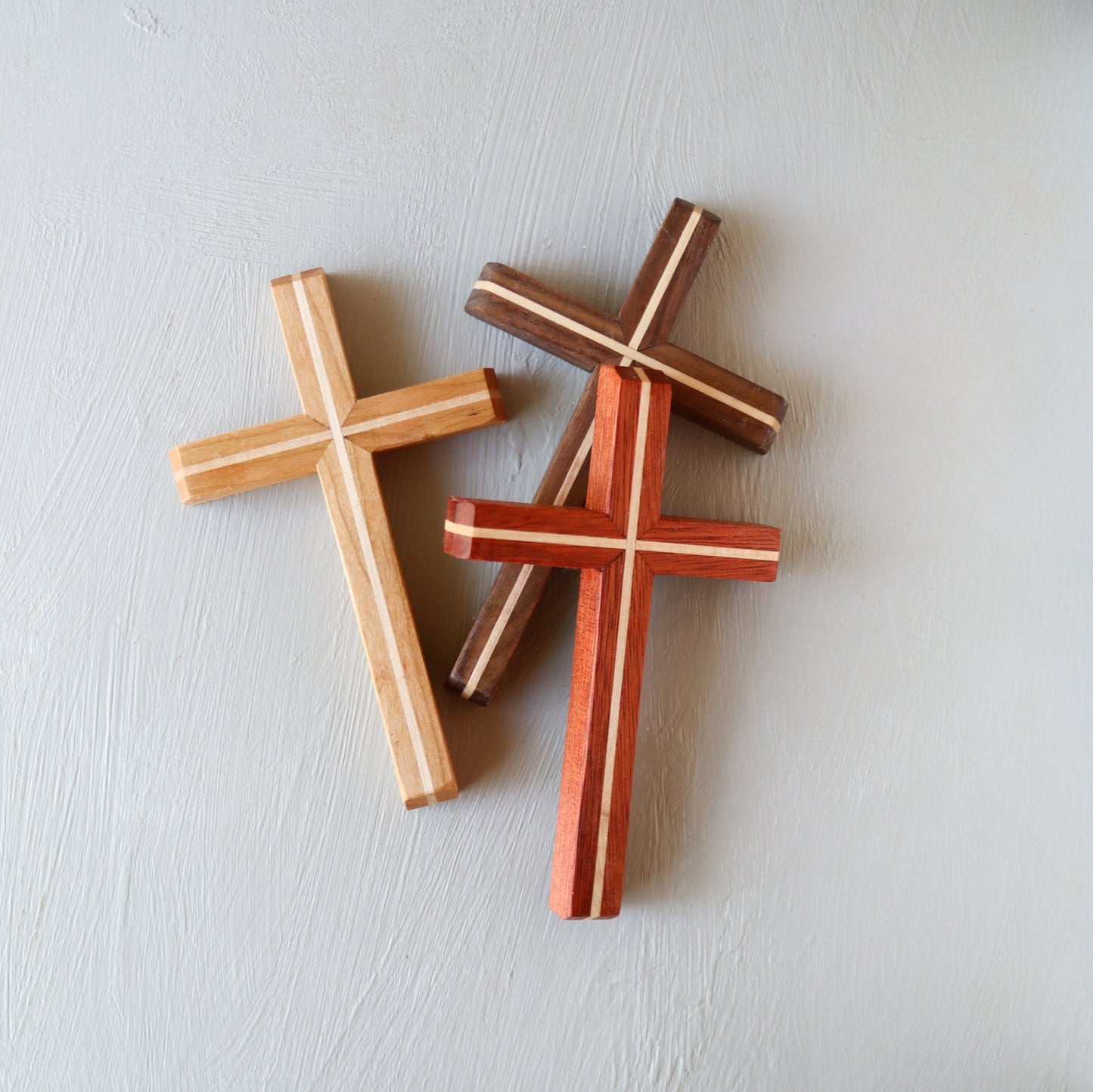 Three handmade wooden Thinline Crosses in different wood tones arranged on a light surface