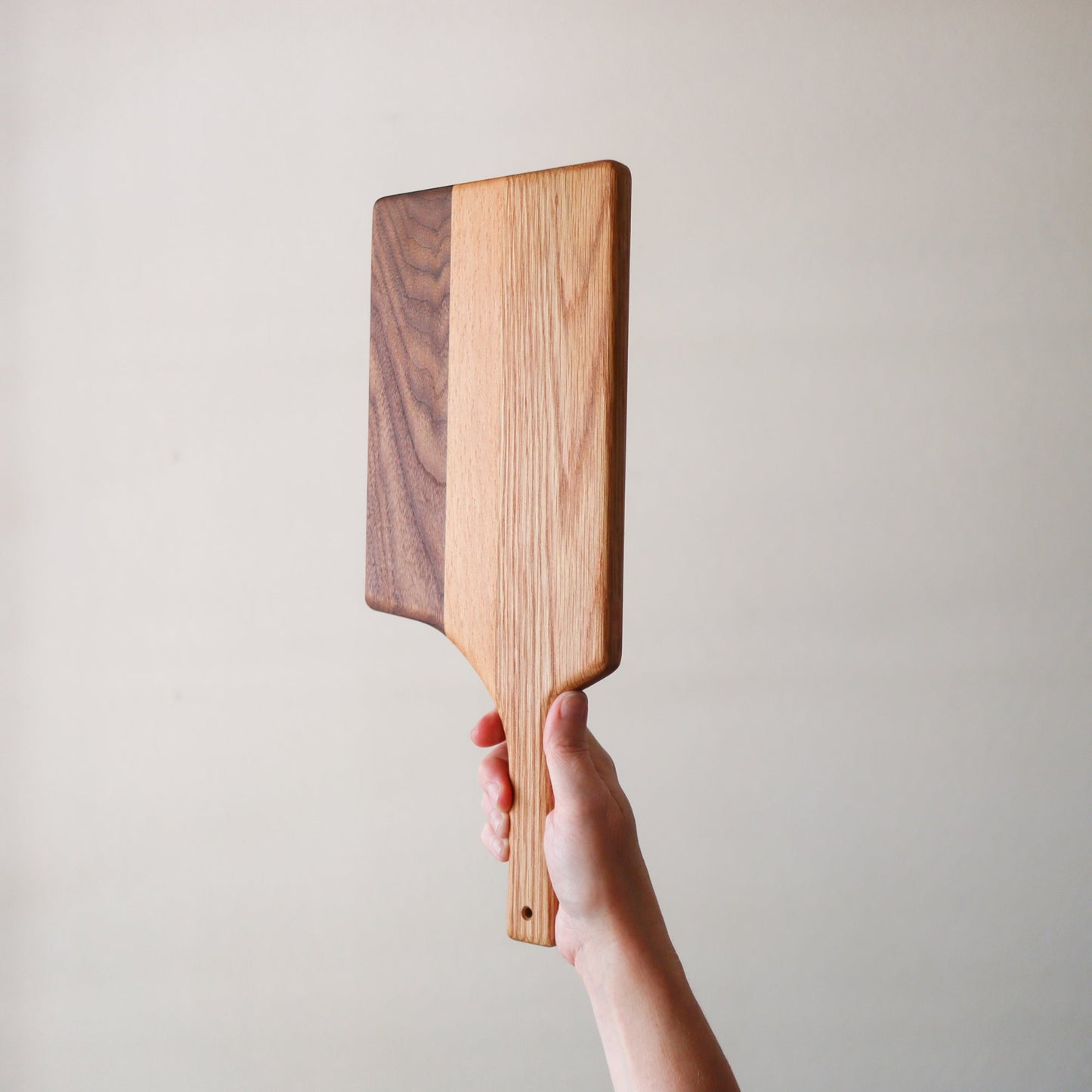 Handheld long handle charcuterie board made from laminated reclaimed hardwood with contrasting light and dark stripes