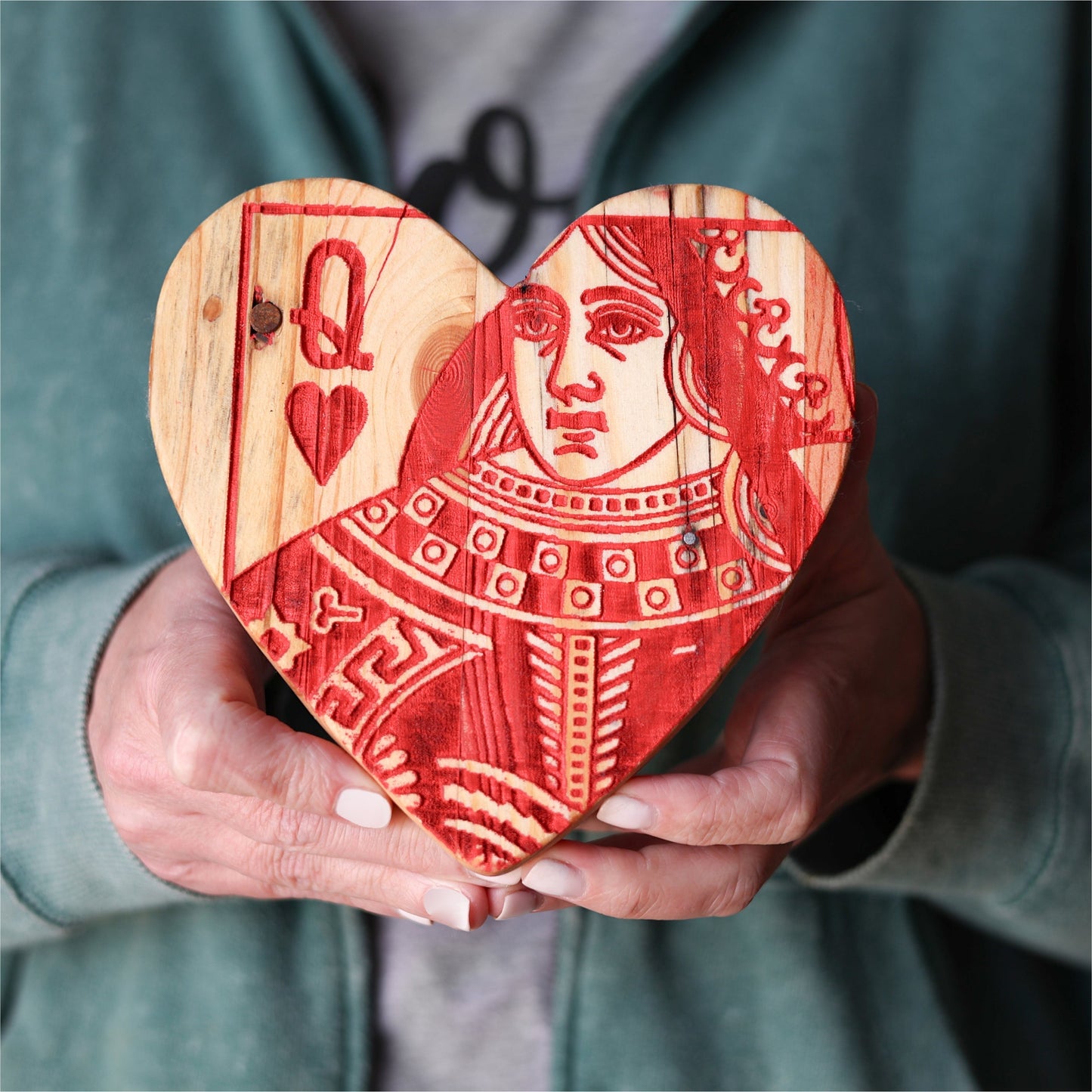 Handcrafted Queen of Hearts wooden heart made from reclaimed pallet wood with red playing card engraving, held in hands.