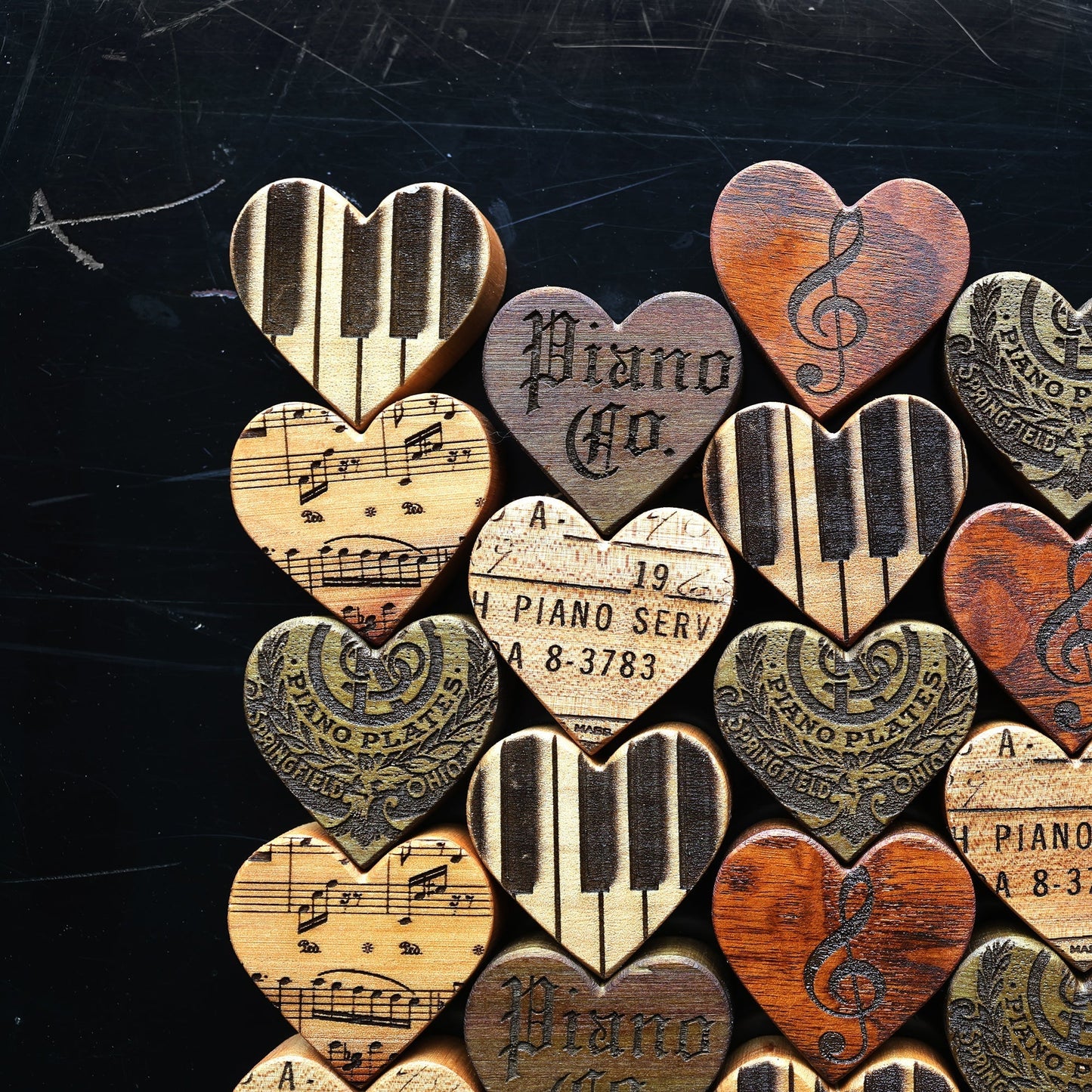 Assorted engraved piano wood hearts featuring piano keys, musical notes, and vintage piano designs made from reclaimed piano wood