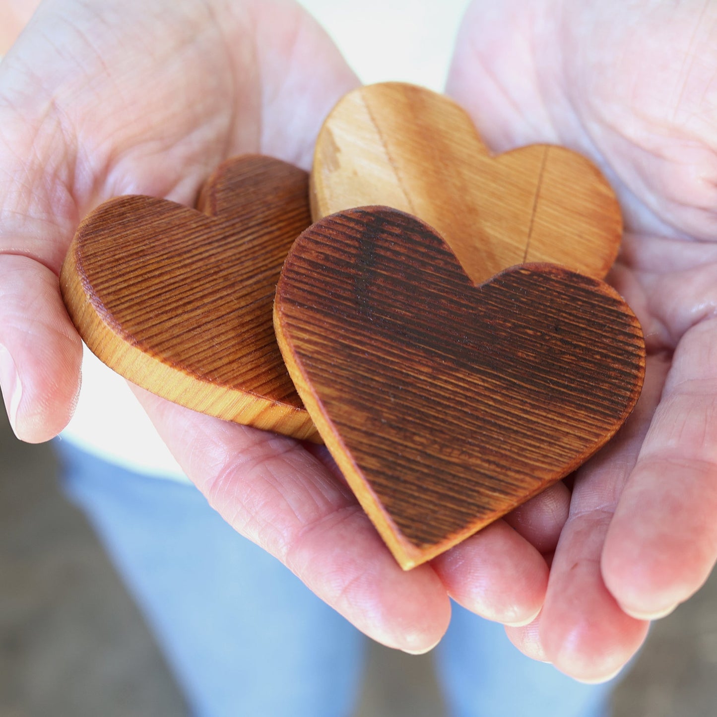 Handcrafted piano soundboard hearts made from reclaimed solid spruce wood, showing natural wood grain and rustic finish in a person's hands.