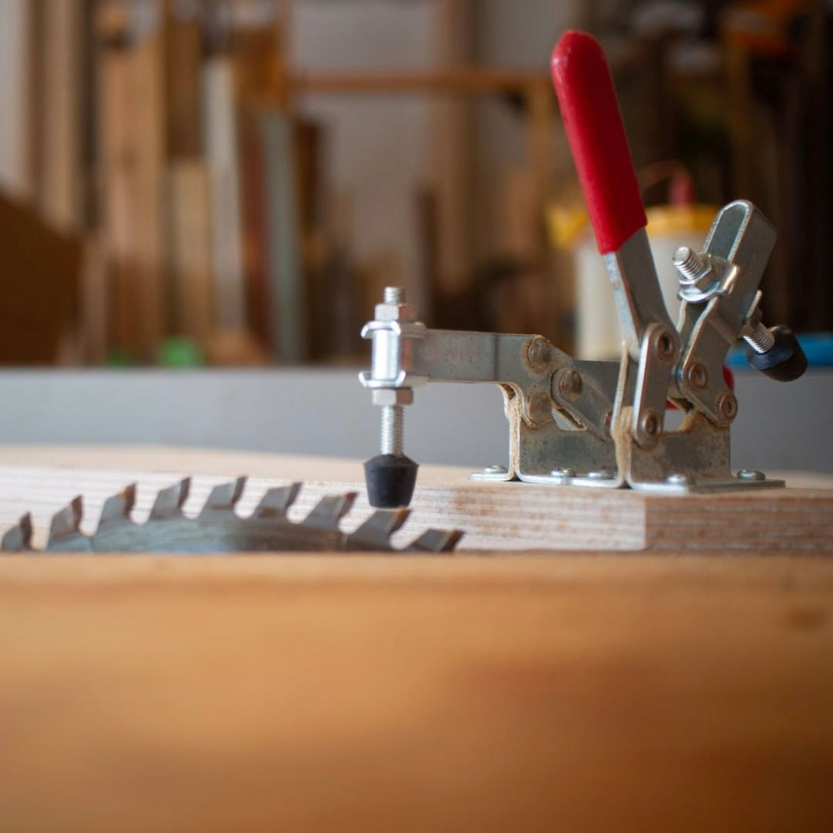 Close-up of a table saw sled jig with a red handle clamping mechanism and a circular saw blade for precise woodworking cuts