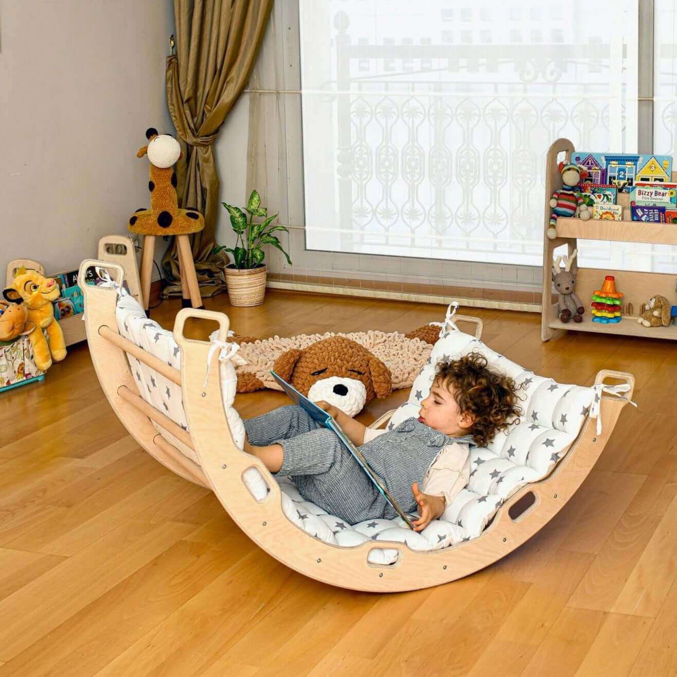 Child relaxing on a white star pillow in a wooden climbing arch rocker indoors playground