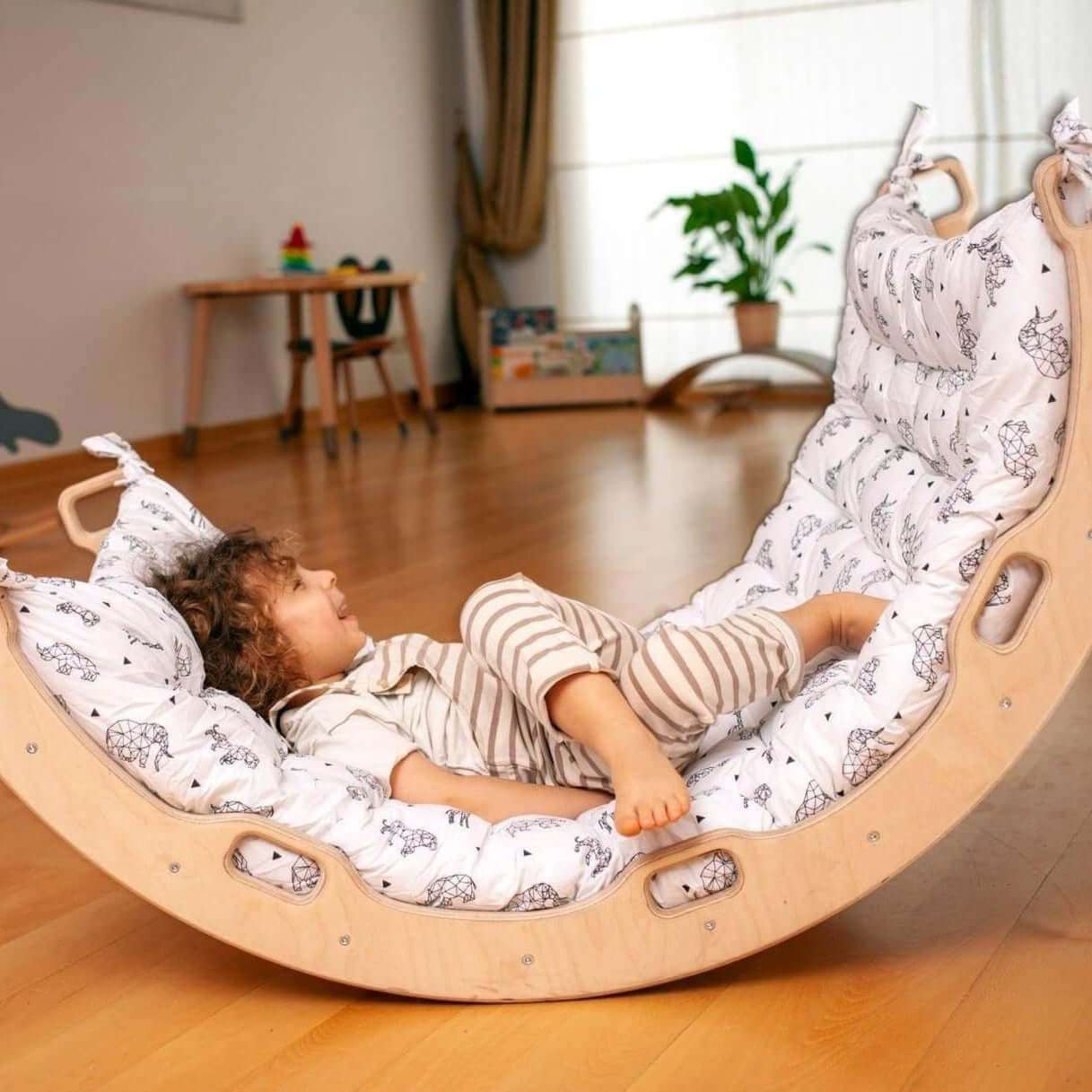 Child playing and reclining on a wooden Climbing Arch Rocker with cushion pillows in a bright room