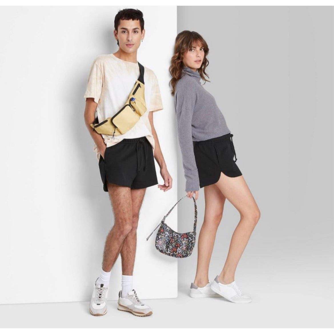 Man and woman wearing black high-rise dolphin shorts with casual tops and sneakers in a studio setting