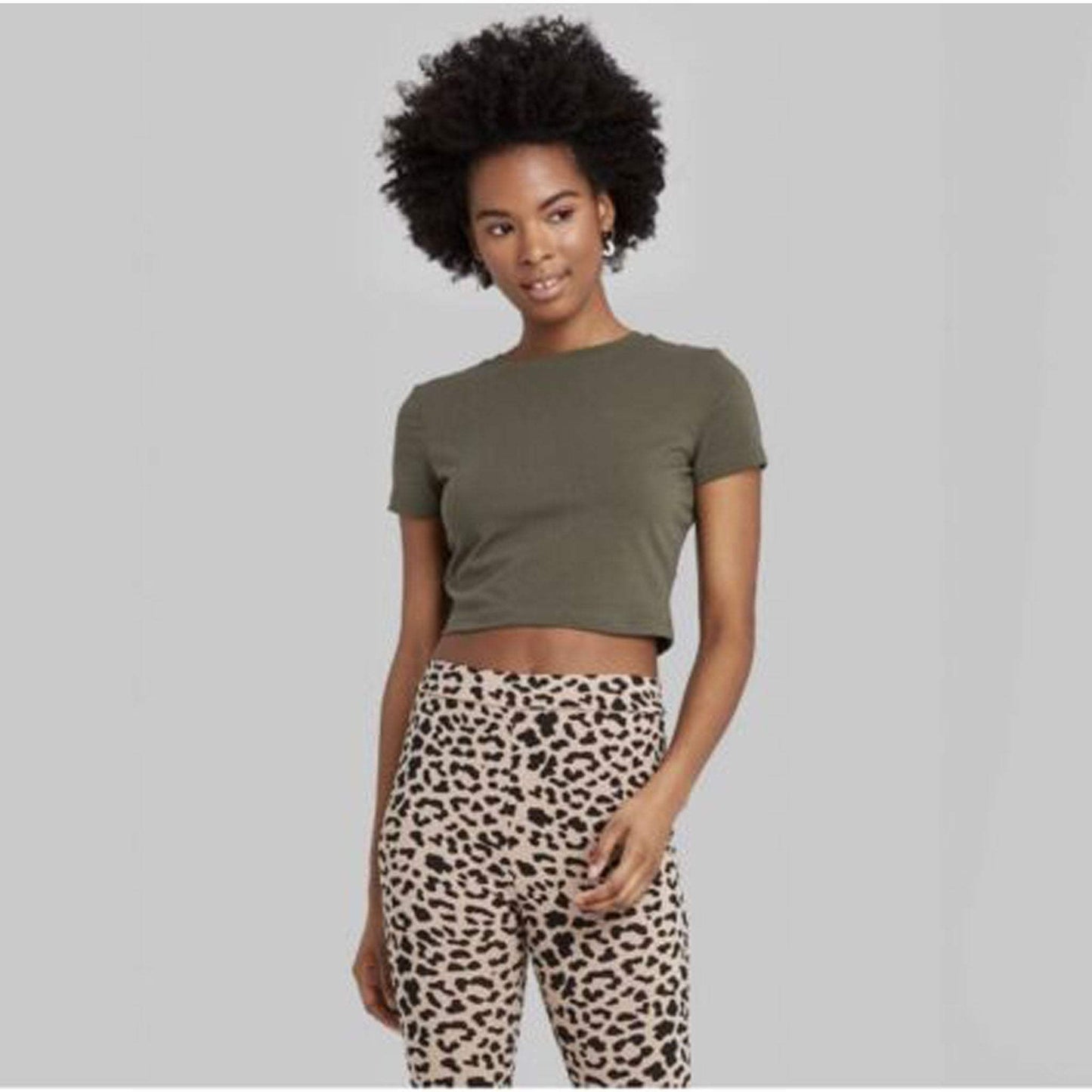 Woman wearing olive green short sleeve cropped t-shirt and leopard print pants against gray background