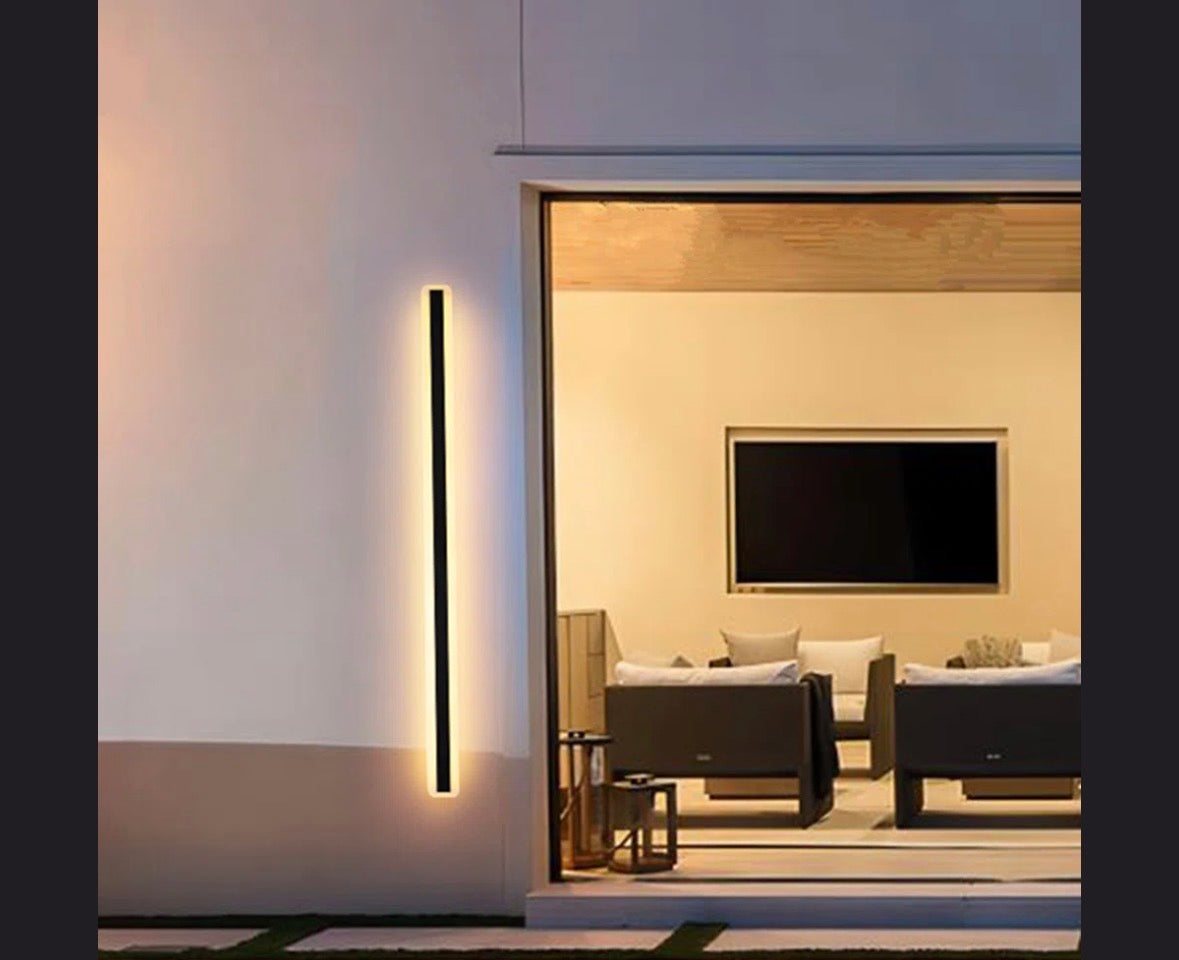 Ivy Bronx Barde Slender sideway outdoor LED wall sconce emitting warm light near patio seating area