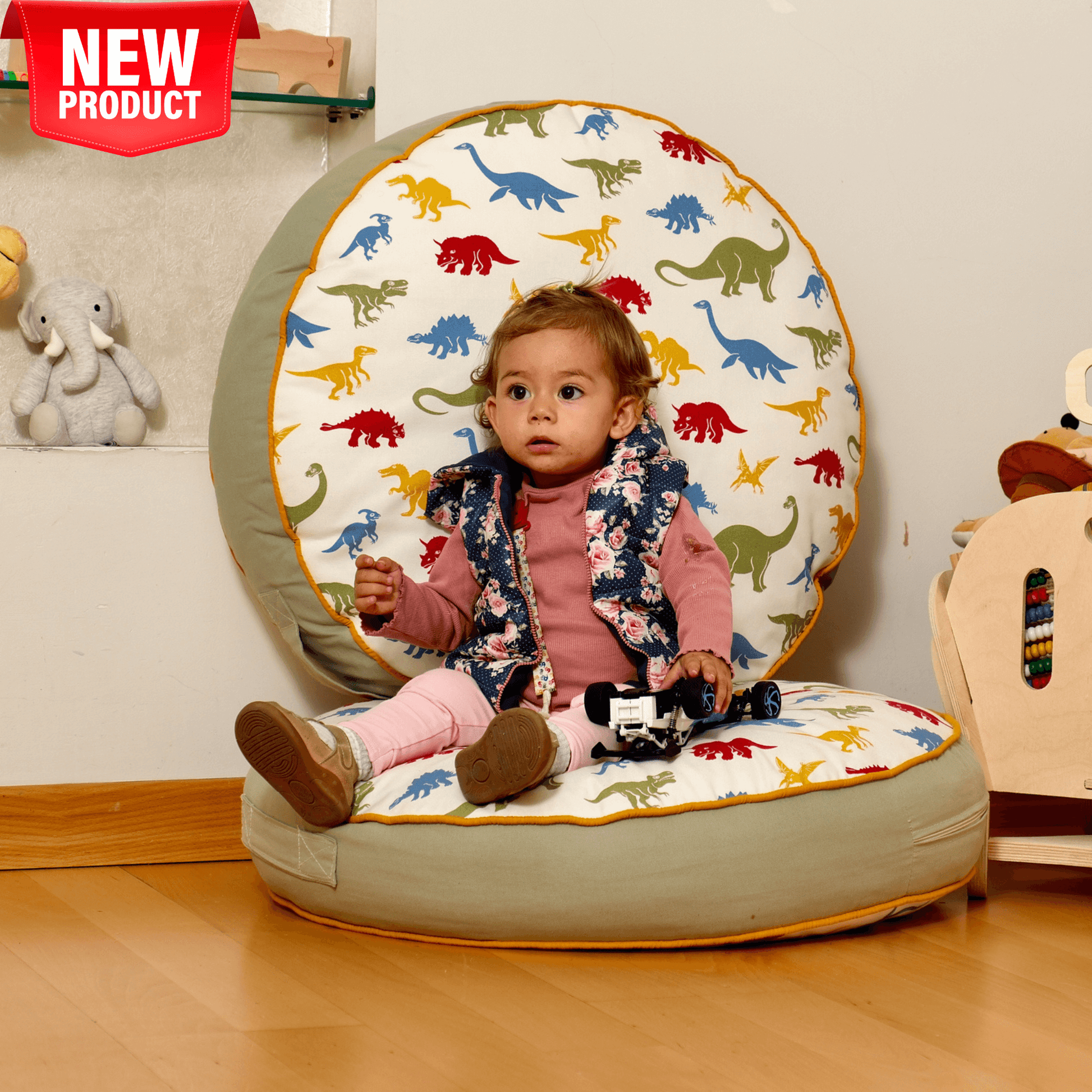 Toddler sitting on a large round kids floor pillow with colorful dinosaur print, soft cotton blend cushion for play, reading, and relaxation.