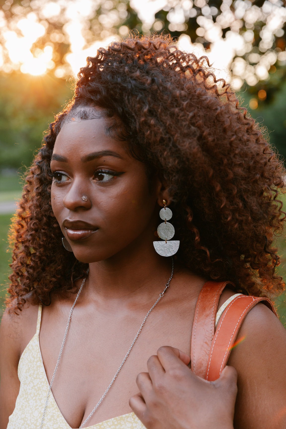 Woman wearing Bateau Earring with geometric upcycled aluminum design and gold-plated posts outdoors at sunset