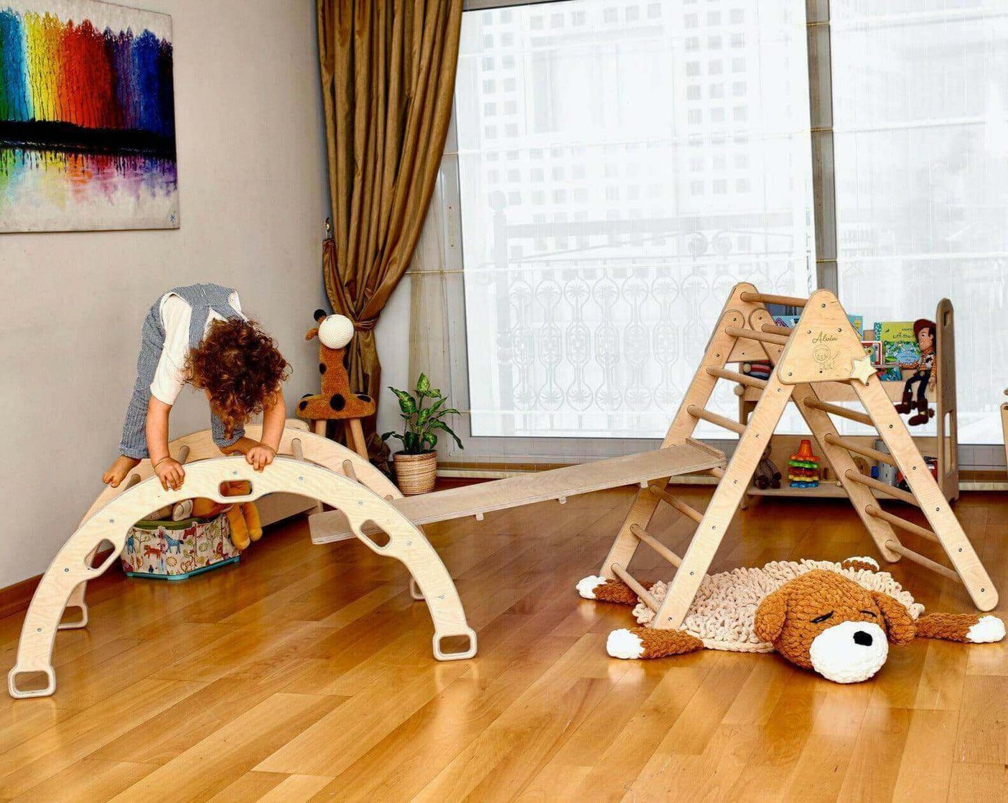 Child playing on a natural wood Montessori climbing set with Pikler triangle, climbing arch, and ramp in a bright indoor room