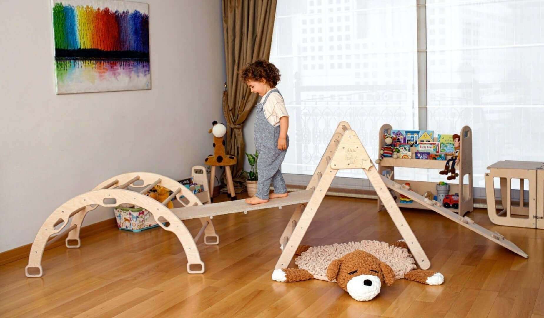 Child playing on a natural wood Montessori climbing triangle with arch and ramps set on a wooden floor indoors