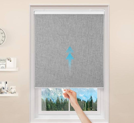 Cordless blackout roller window shade installed on window with hand adjusting height, gray thermal insulated fabric, UV protection and privacy features.