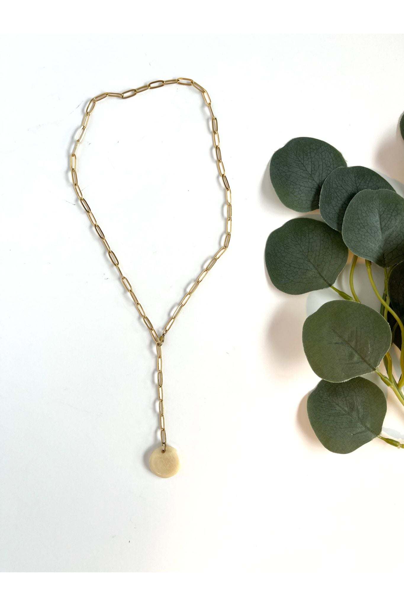 Alana Necklace gold-plated paper clip chain with horn pendant on white background next to green leaves