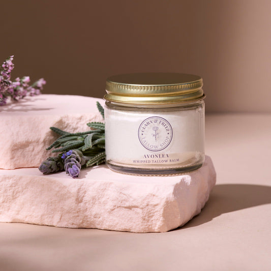 Avonlea Chamomile and Lavender Whipped Tallow Balm in glass jar with gold lid on pink stone slab with lavender and green leaves background