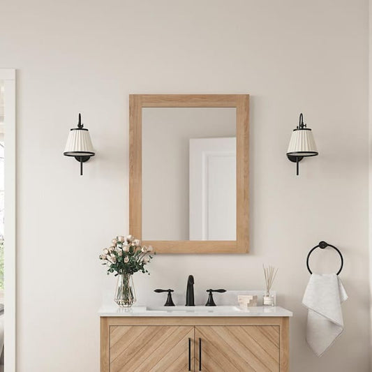 Glacier Bay Huckleberry 24x32 inch rectangular framed bathroom vanity mirror in weathered tan wood finish mounted above a bathroom sink with black fixtures and wall sconces.