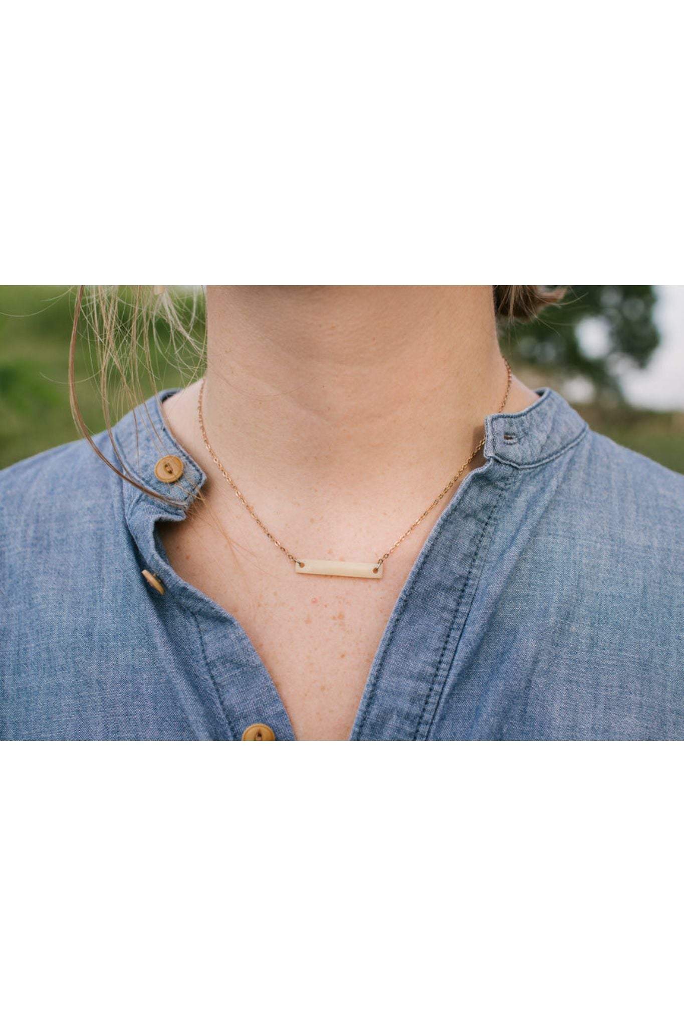 Betty Bone Necklace by Atelier Calla on a person wearing a blue shirt with an adjustable gold chain and a rectangular bone pendant.