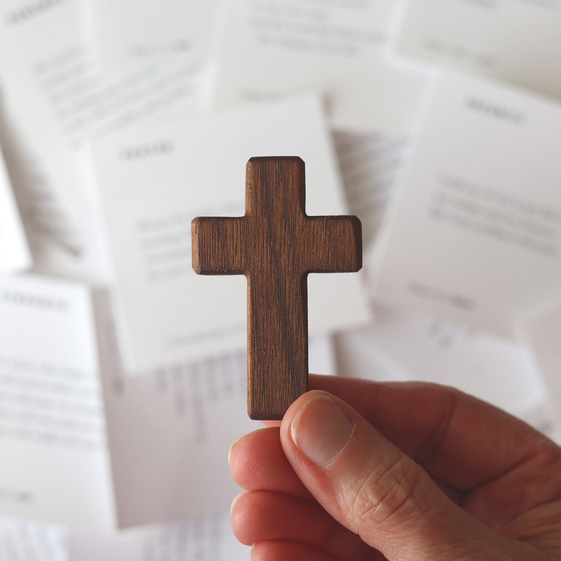 Hand holding a small wooden cross with blurred Bible memory cards in the background