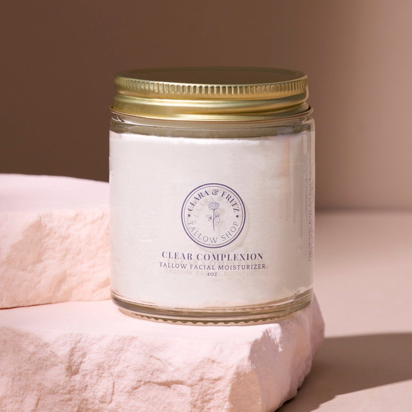 Clear Complexion Whipped Tallow facial moisturizer in glass jar with gold lid on soft pink stone background
