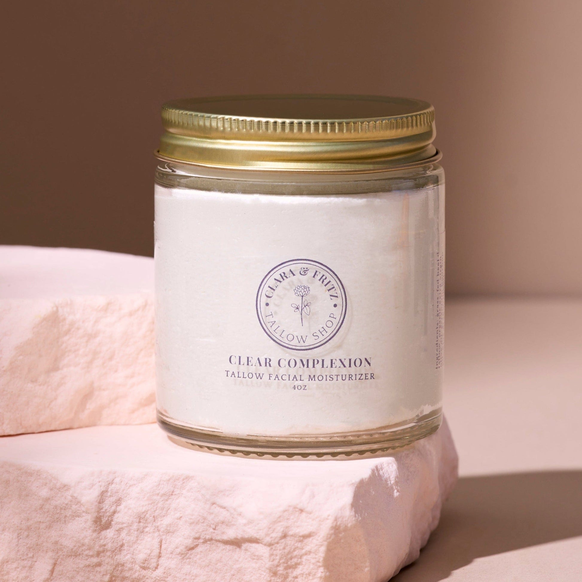 Clear Complexion Whipped Tallow facial moisturizer in glass jar with gold lid on soft pink stone background