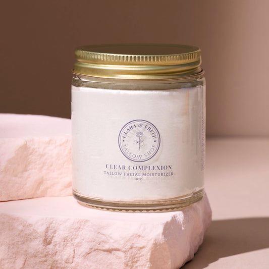 Clear Complexion Whipped Tallow facial moisturizer in glass jar with gold lid on soft pink stone background