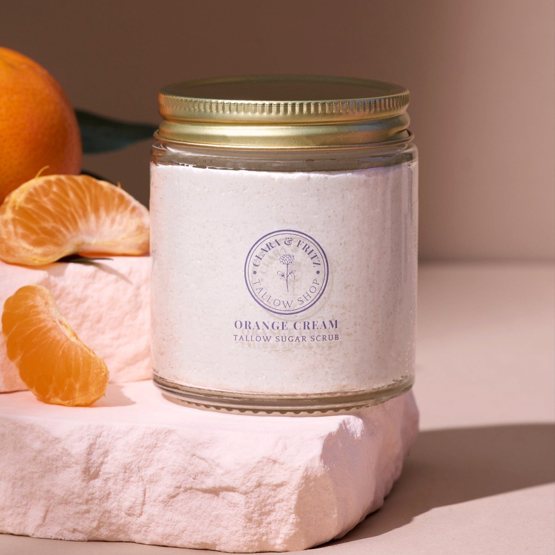 Jar of Orange Cream Sugar Scrub with tallow, sitting on stone slab next to orange slices and whole orange