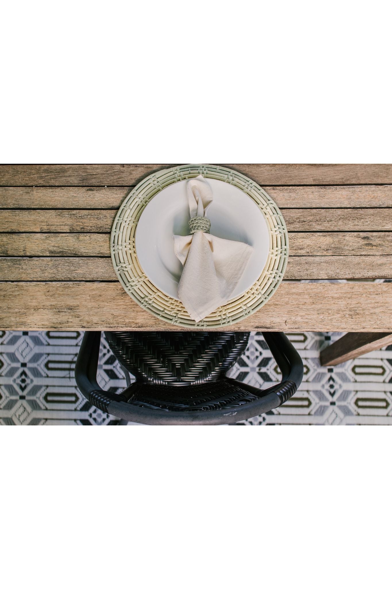 Round trivet placemat with sage green edge, woven palm leaf design, and neutral napkin on rustic wooden table.