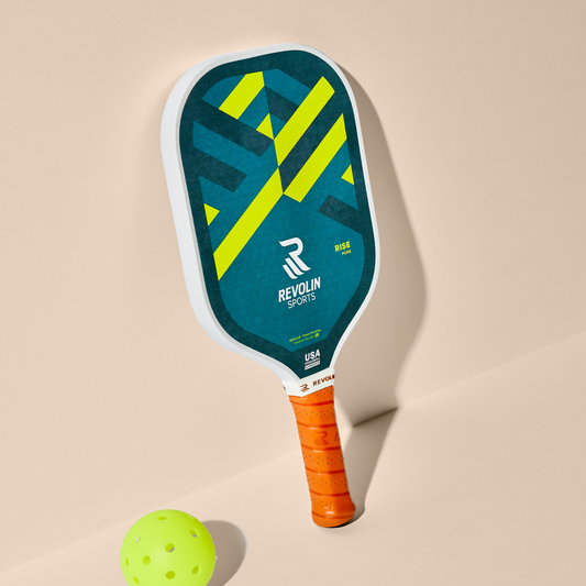 Rise Pickleball Paddle with blue and green design, ergonomic orange handle, and textured matte finish next to yellow pickleball ball