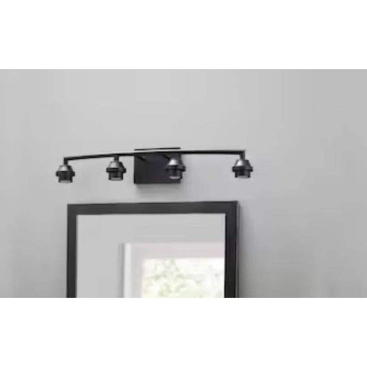 Black 4-light vanity fixture above a mirror in a bathroom setting.