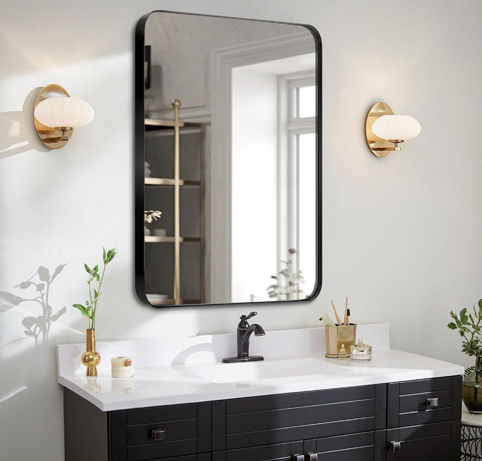 24x36 inch black bathroom mirror with aluminum alloy frame mounted above white sink vanity with gold wall sconces and plants