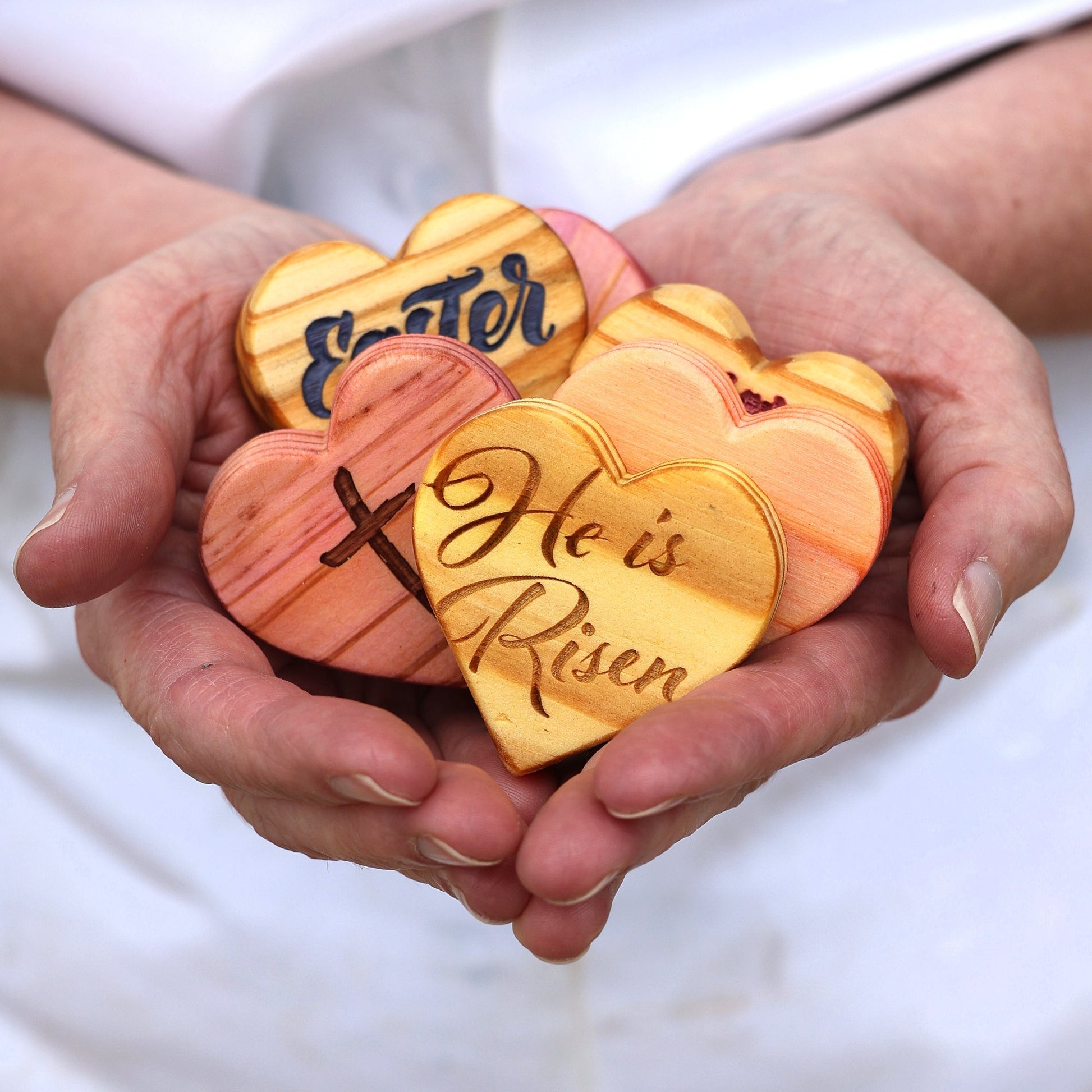 Hands holding handmade engraved wooden Easter hearts with religious messages and symbols, crafted from reclaimed wood.