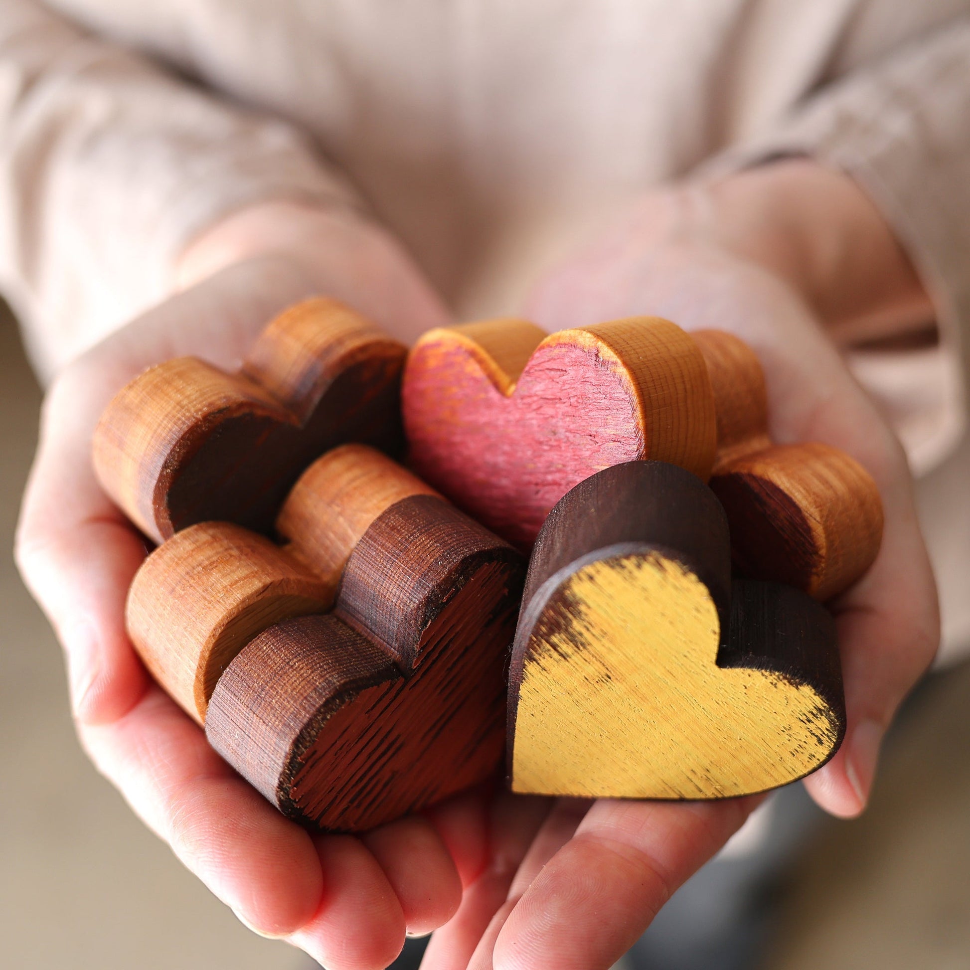 Hands holding six handmade wooden hearts with fall-inspired colors and finishes from the Fall Flare 2024 collection