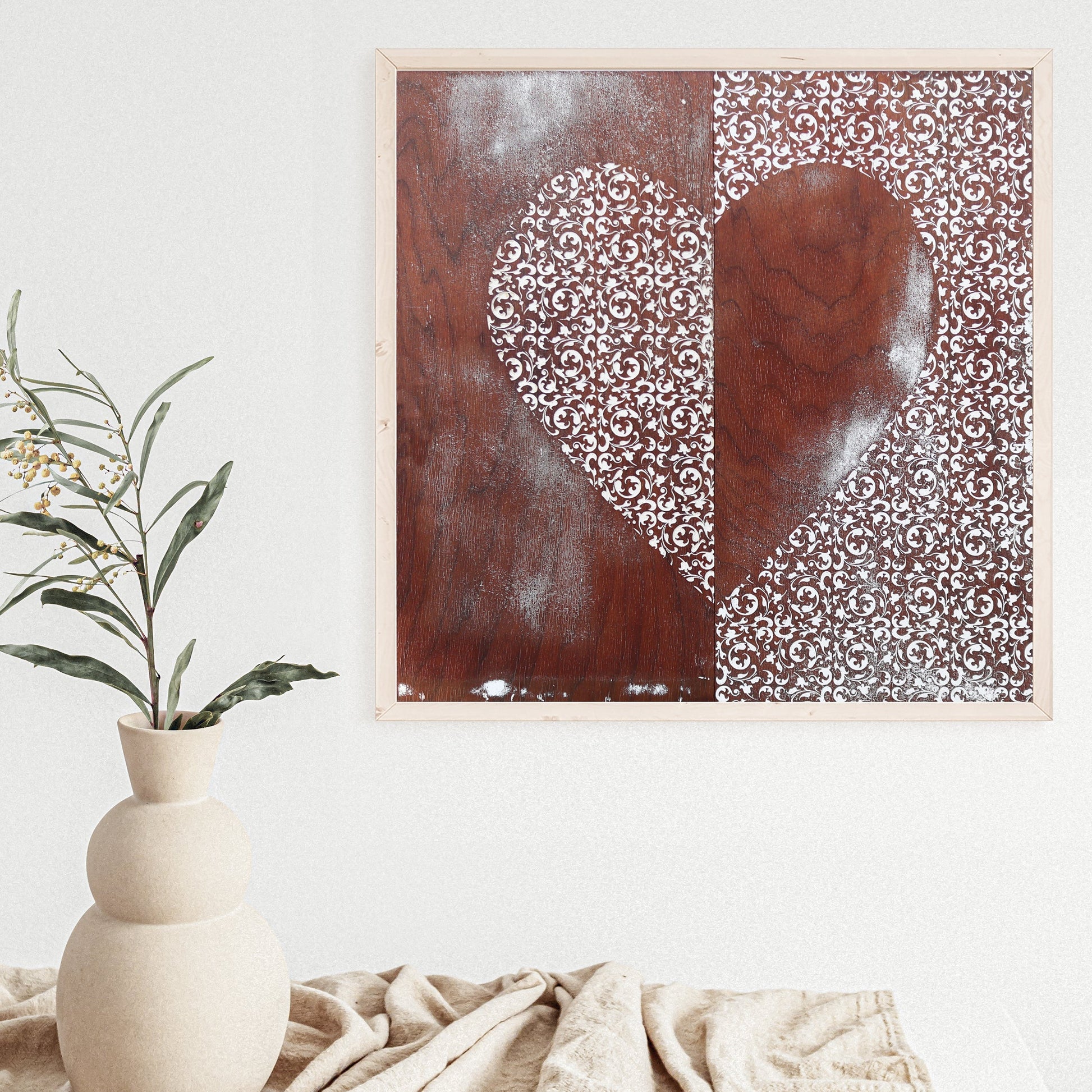 Square Heart of Filigree Art Print with intricate yin and yang-inspired patterns in brown and white wood tones, framed and hung on a white wall above a beige textured cloth and vase with green foliage