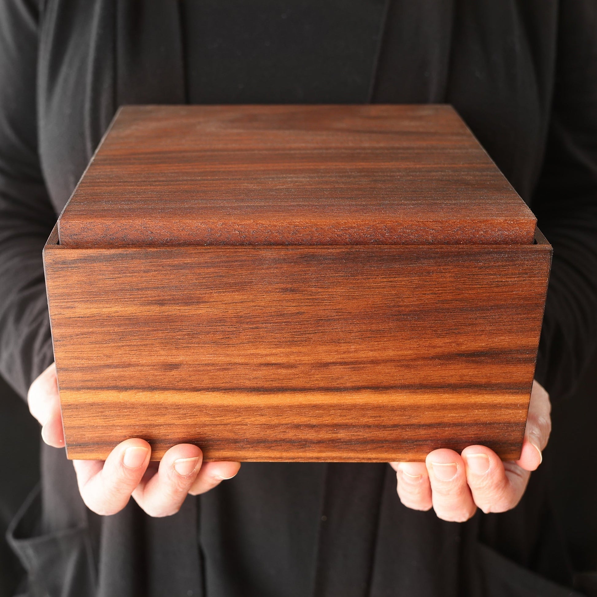 Handcrafted walnut wood Forever Box held by person in black attire, showcasing smooth grain and rectangular shape
