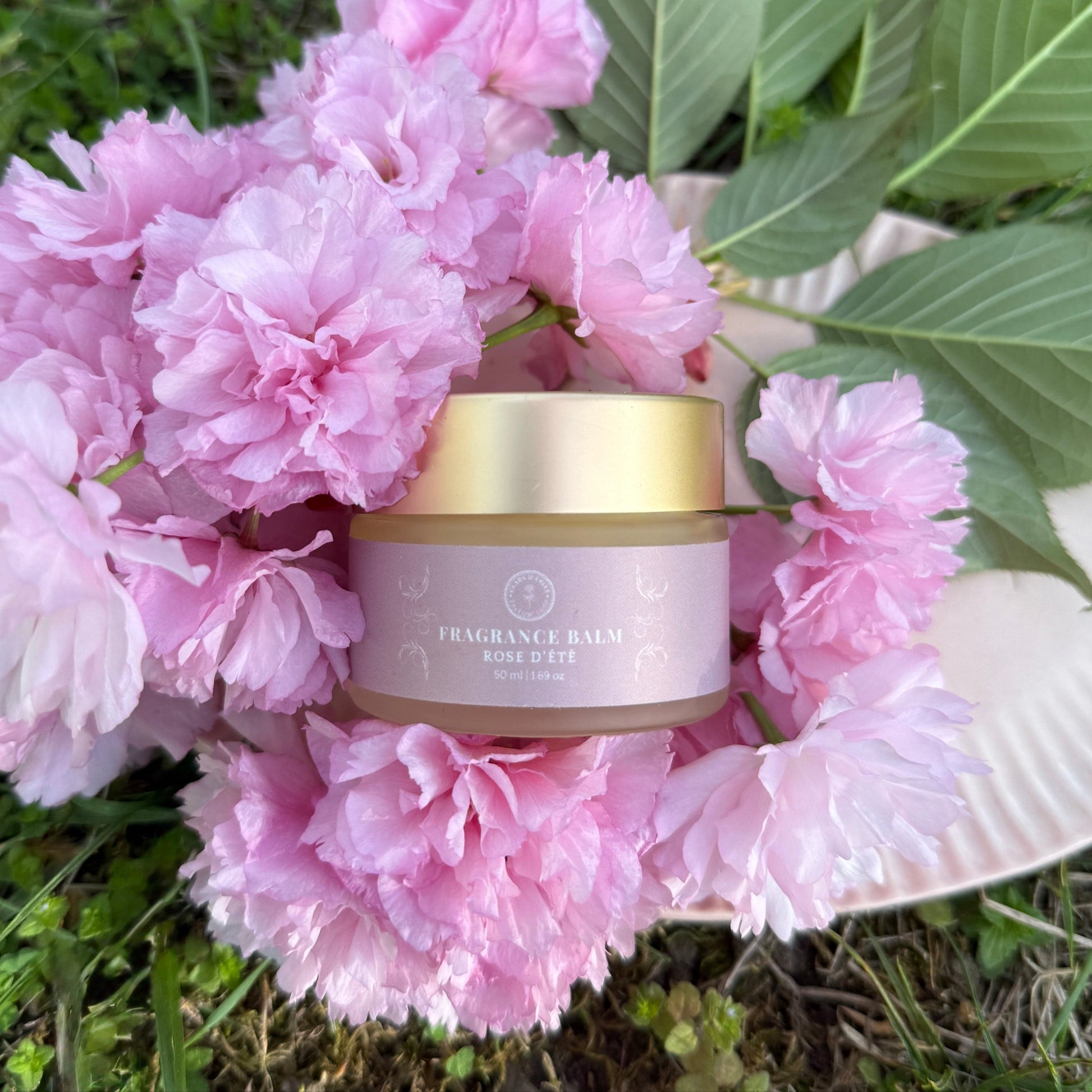 Fragrance Balm with rose and bergamot scent in a jar surrounded by pink flowers