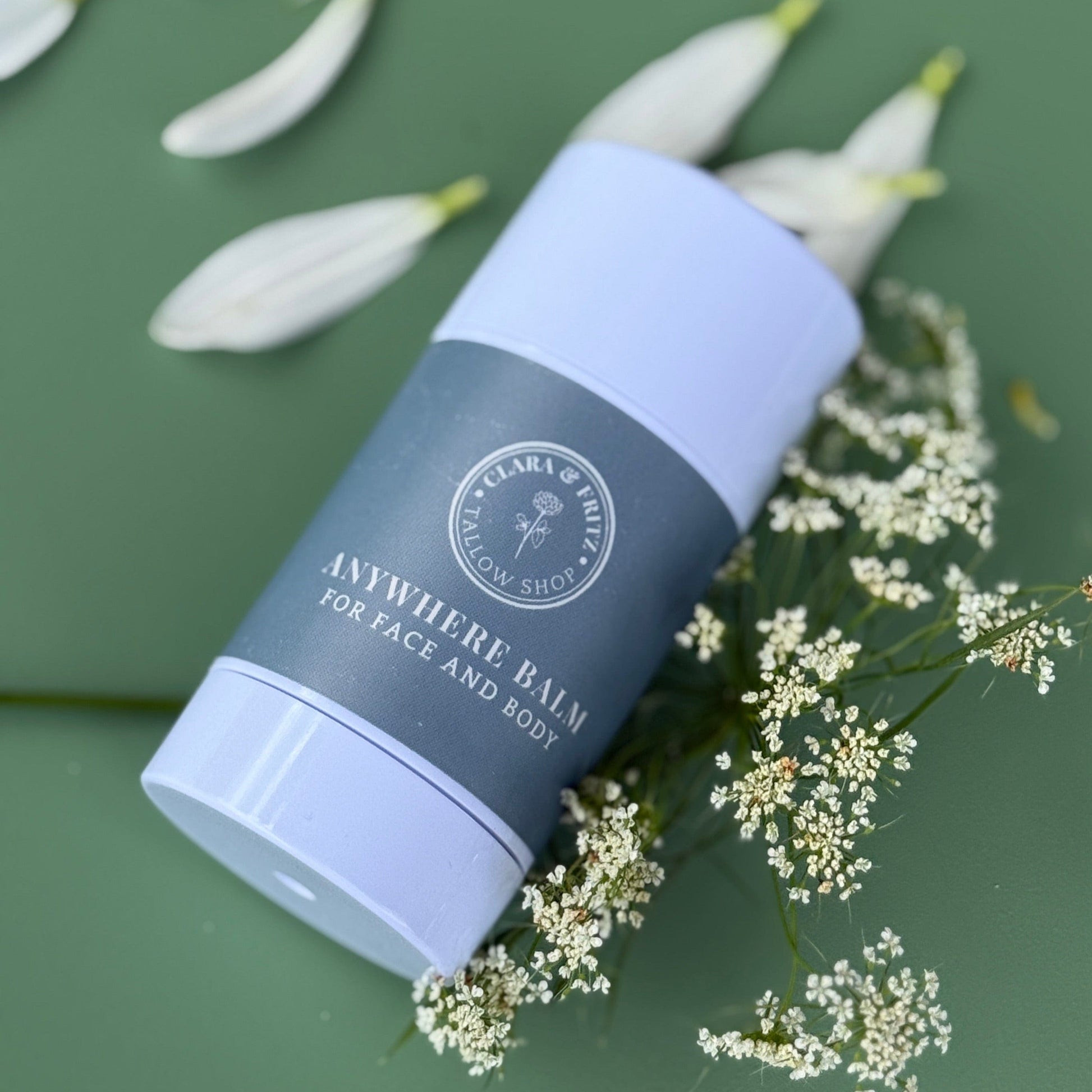 Anywhere Balm for Face and Body moisturizing stick surrounded by white flowers on green background