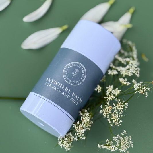 Anywhere Balm for Face and Body moisturizing stick surrounded by white flowers on green background