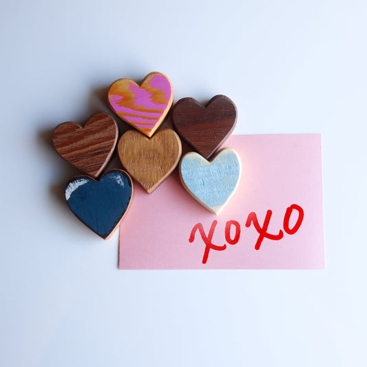 Set of colorful reclaimed wooden heart magnets holding a pink card with "xoxo" written in red.