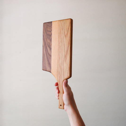 Handheld long handle charcuterie board made from laminated reclaimed hardwood with contrasting light and dark stripes
