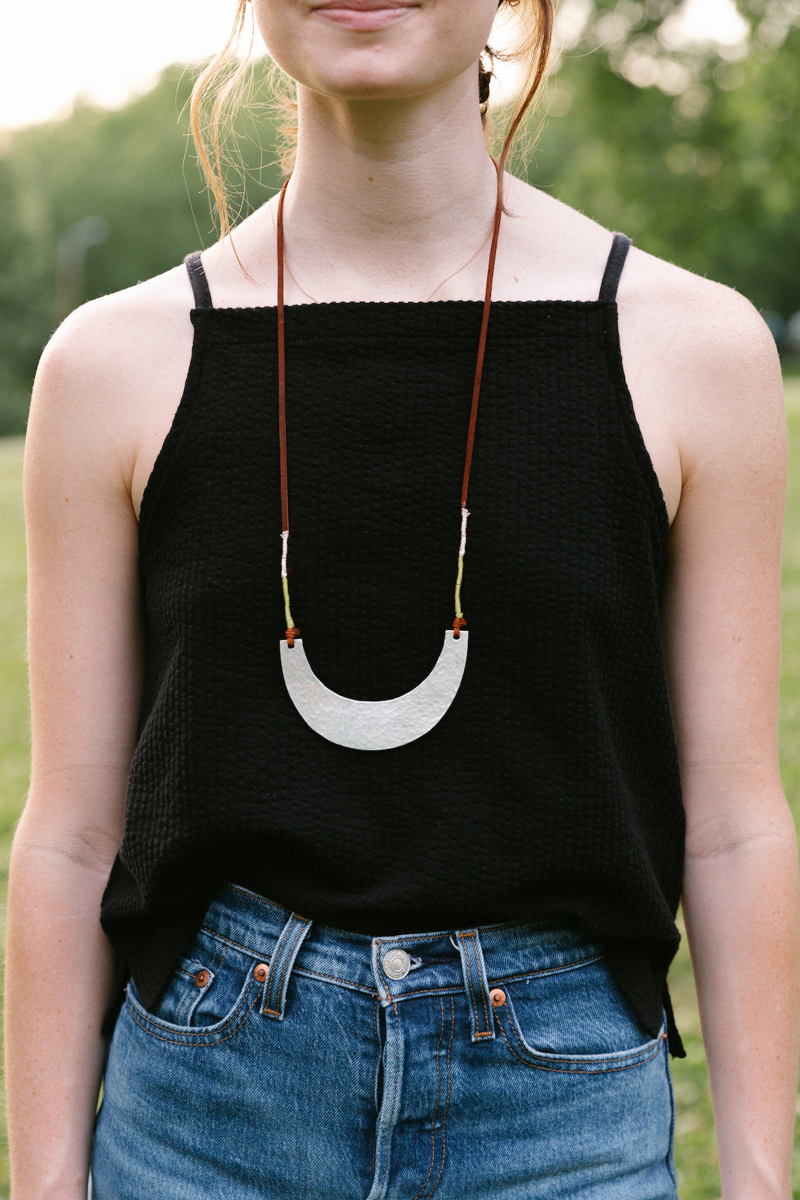 Woman wearing hammered scoop necklace with leather cord and upcycled aluminum pendant over black top