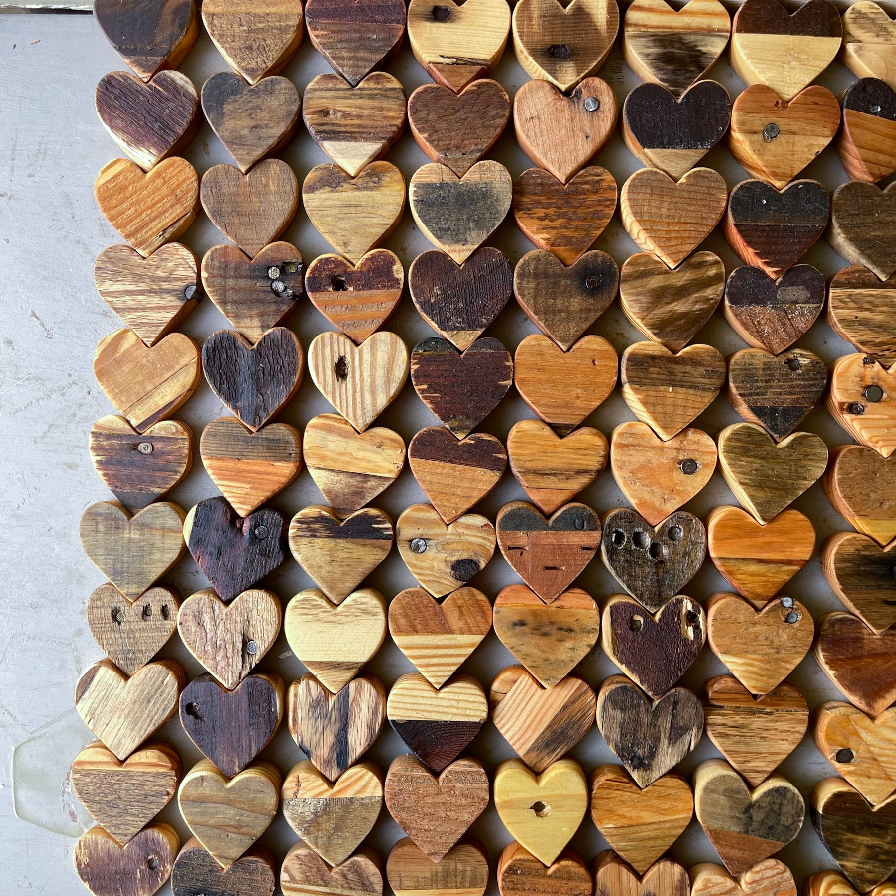 Collection of reclaimed pallet wood hearts in various natural wood tones and rustic finishes arranged in neat rows on a gray surface