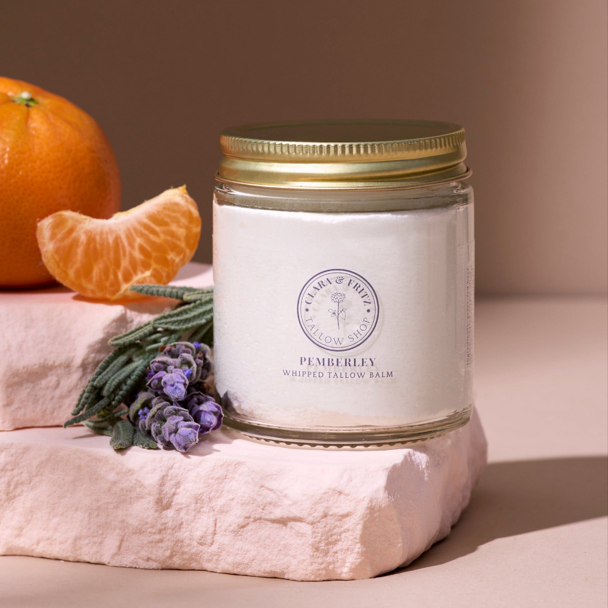 Pemberley Orange and Lavender scented whipped tallow balm in glass jar with orange slice and lavender flowers on stone blocks