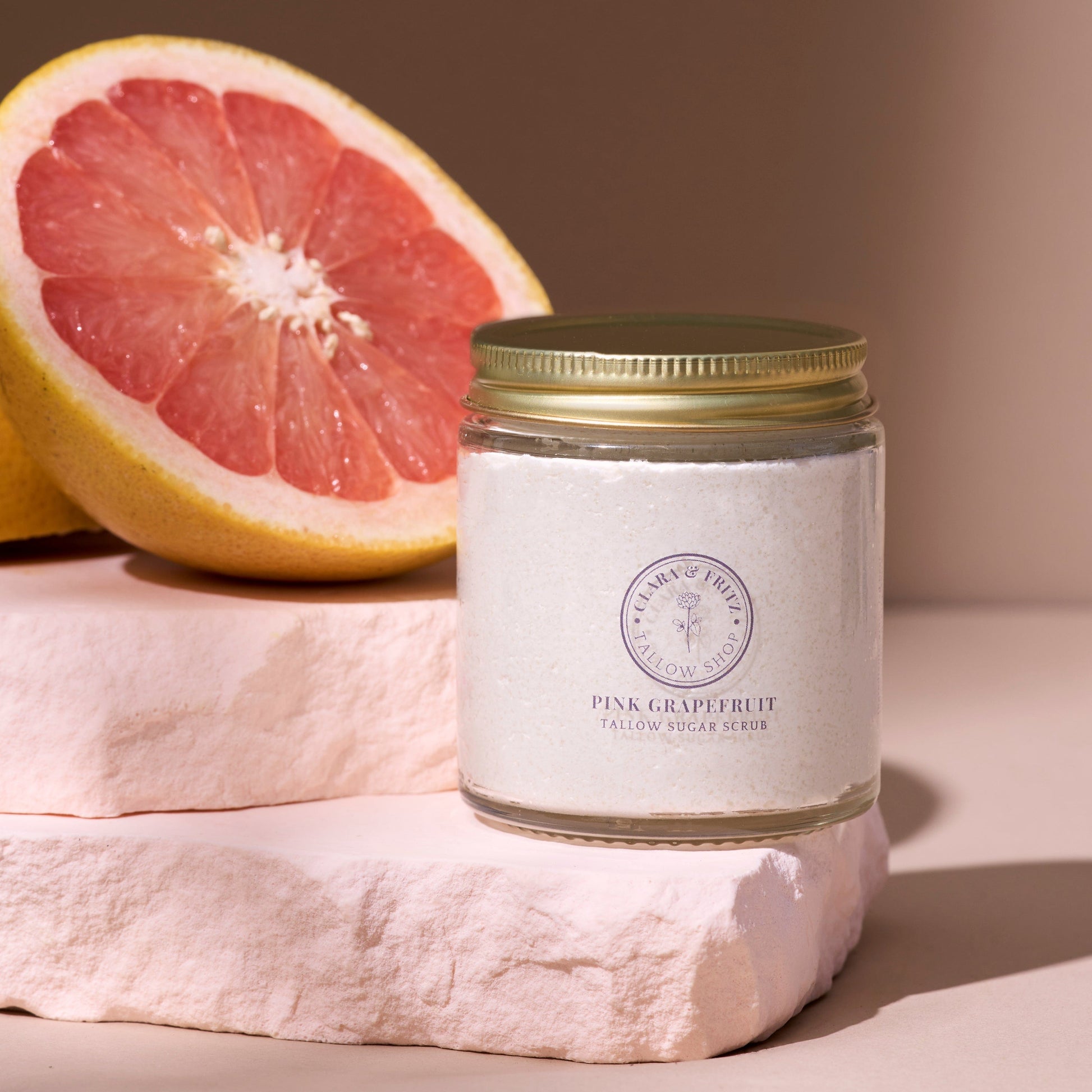 Pink Grapefruit Tallow Sugar Scrub jar with pink grapefruit half and natural stone background