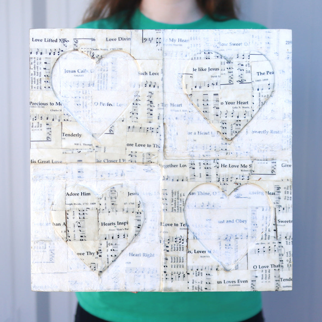 Love Hymns Artwork featuring four heart shapes made from vintage hymnal sheet music on reclaimed piano wood soundboard with acrylic paint and decoupage.