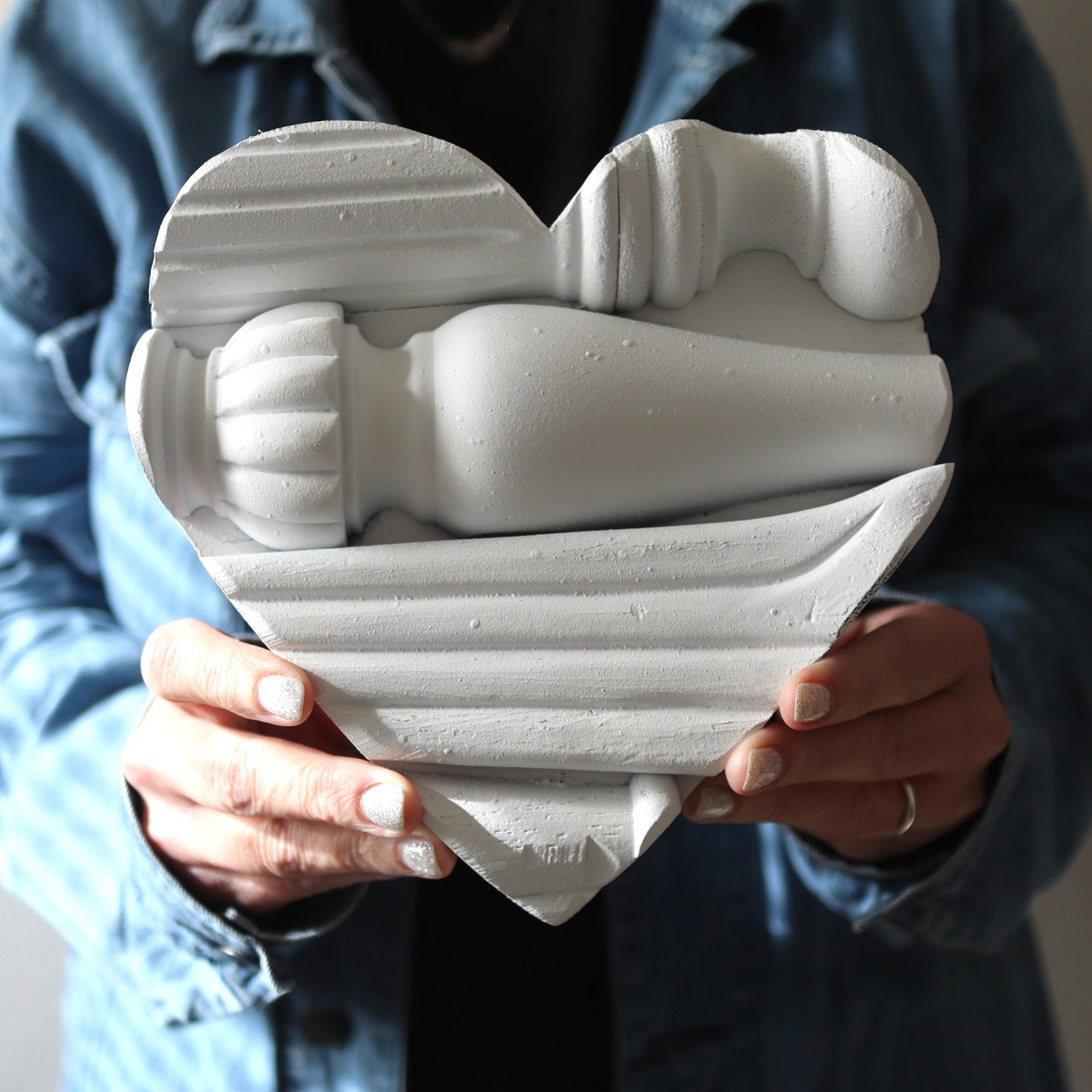 Handmade white Piano Spindle Heart art piece crafted from reclaimed antique piano wood held by person in denim jacket