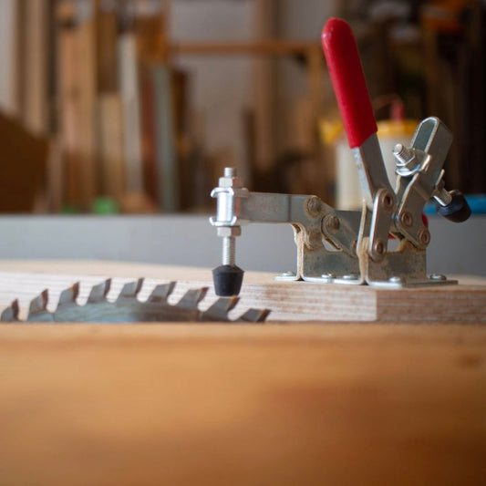 Close-up of a table saw sled jig with a red handle clamping mechanism and a circular saw blade for precise woodworking cuts
