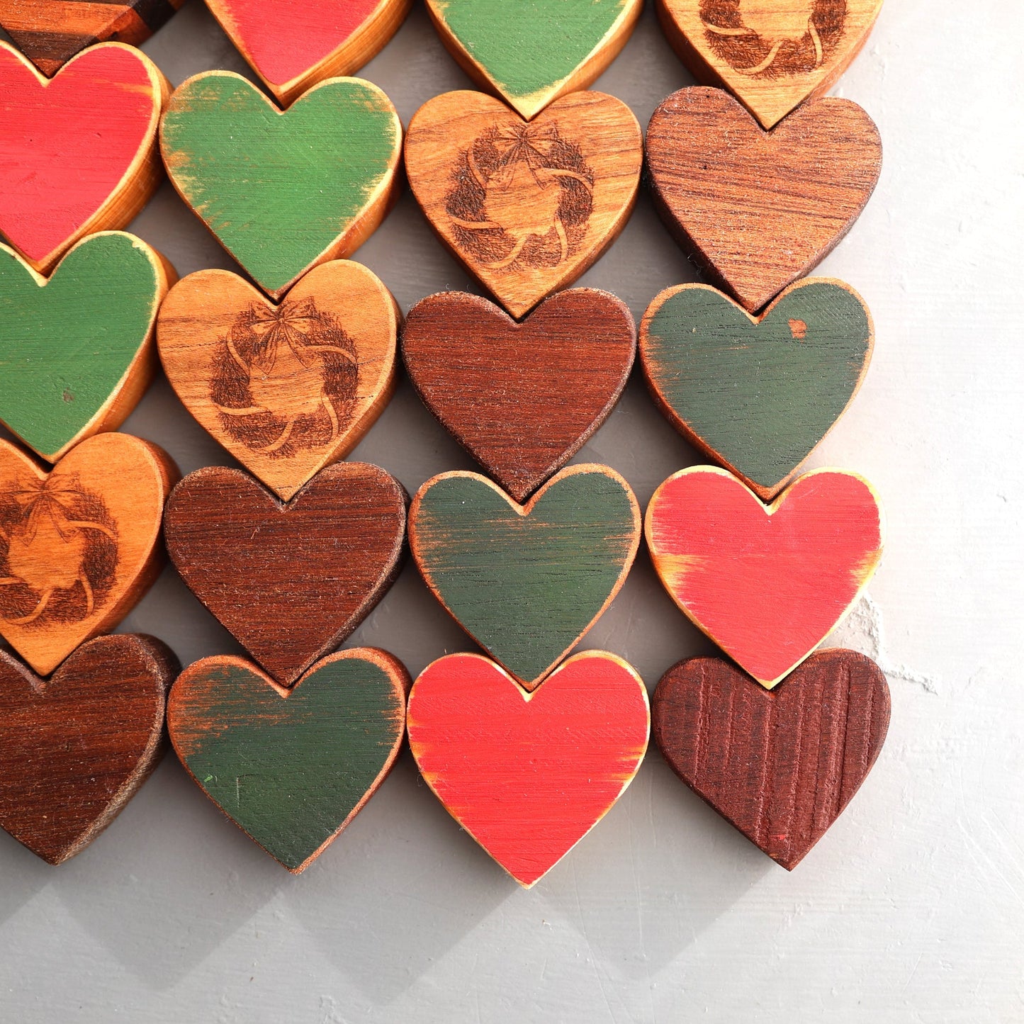 Set of handmade Christmas Hearts in red, green, and natural wood tones with engraved wreath designs for festive holiday decor
